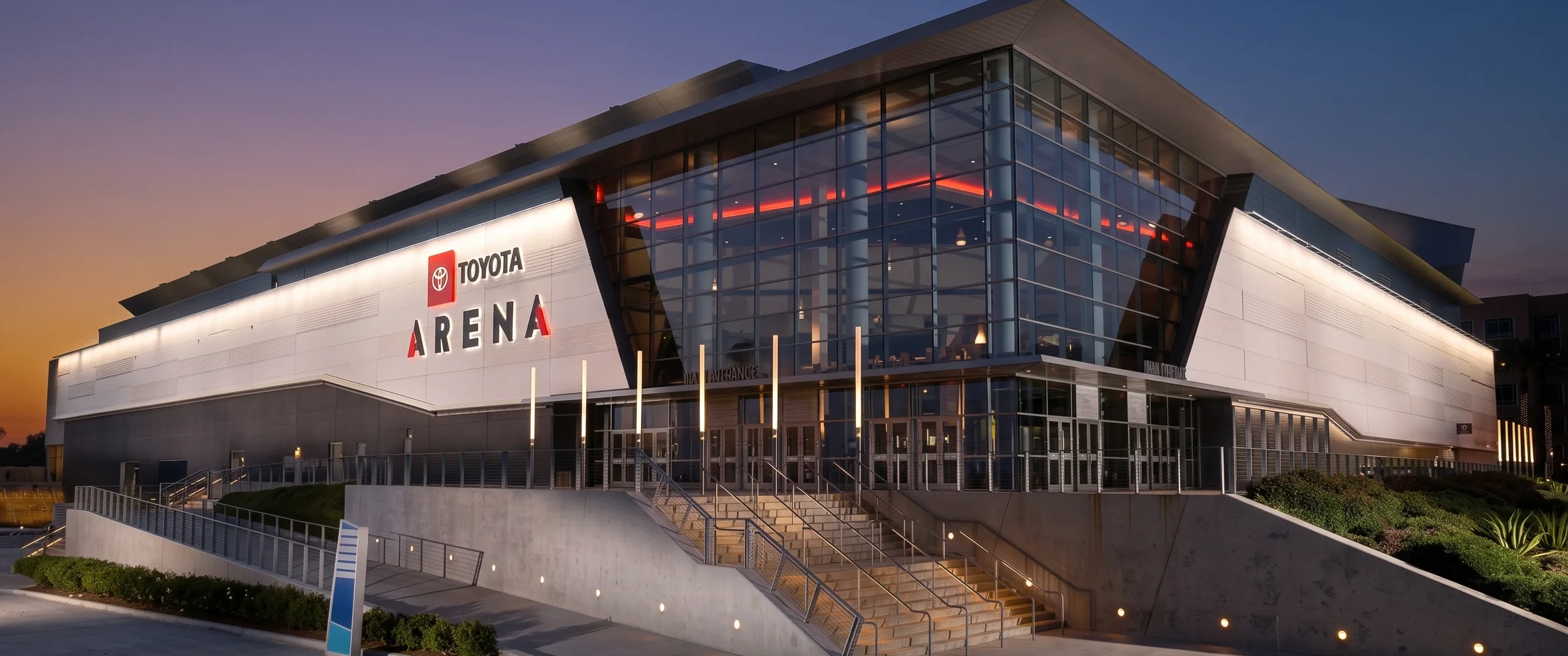 Toyota Arena at dusk: the glass entrance, the illuminated facade and the stairs up to the doors